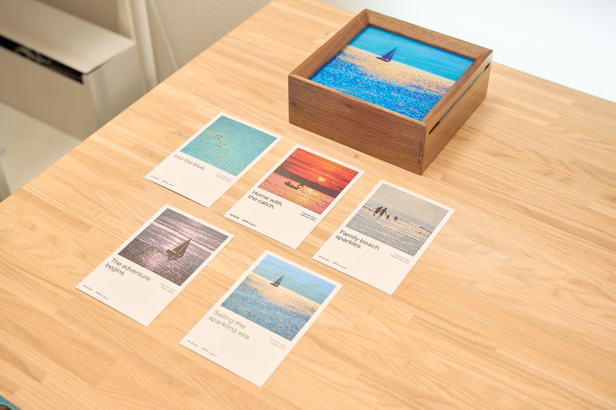 PITAKA 浮光躍金 アーティストコレクション ギフトボックス(青月夢 / Lucid Blue)のライトアートパネルと記念ポストカードを並べている